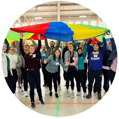 Trainees holding up parachute over their heaids and smilng at he camera in a gym